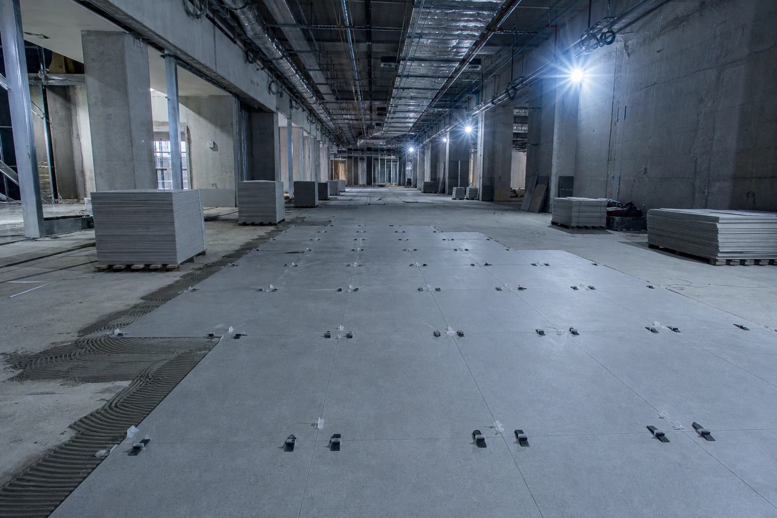 A commercial corridor mid-construction with large-format tile partially installed and pallets staged.